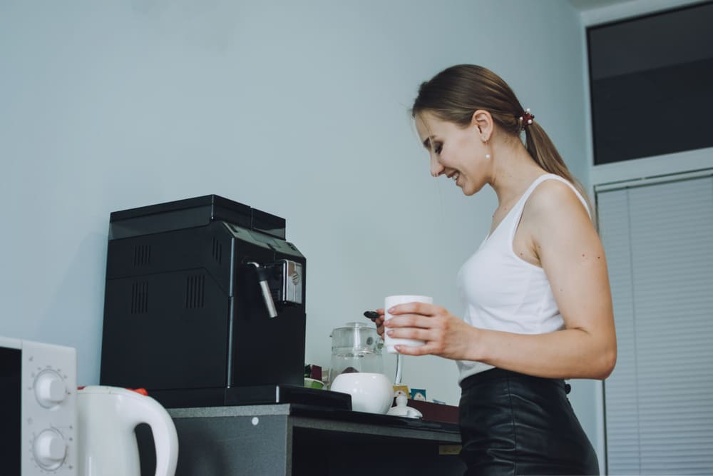 Kobieta (trzymając czajnik bezprzewodowy) wlewa wodę do kubka i przygotowuje sobie kawę z magnezem.  